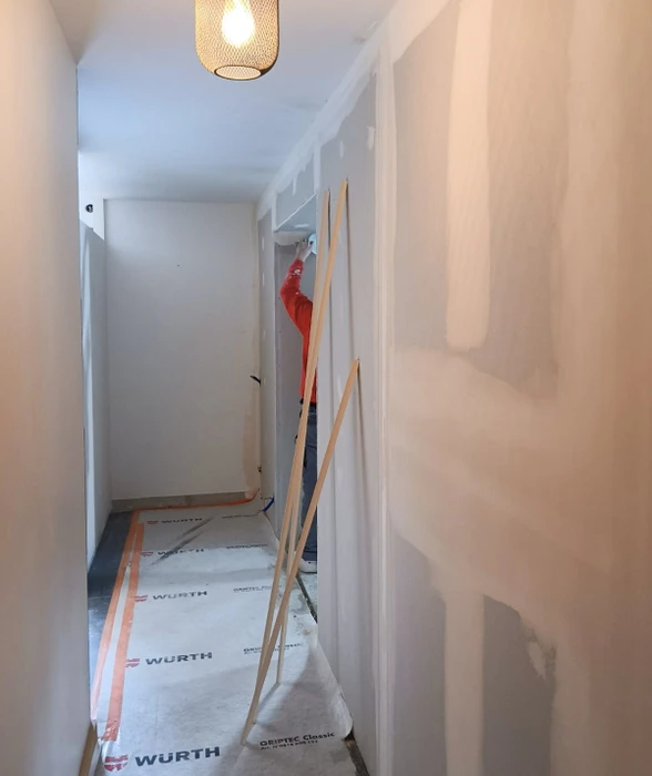 Couloir résidentiel en cours de rénovation avec ouvrier en vêtement rouge travaillant sur échelle pliante