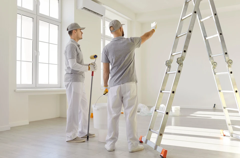 Vue arrière de deux peintres masculins planifiant la rénovation de l'appartement, tenant un rouleau à peinture, travaillant sur l'amélioration de la maison ou la rénovation