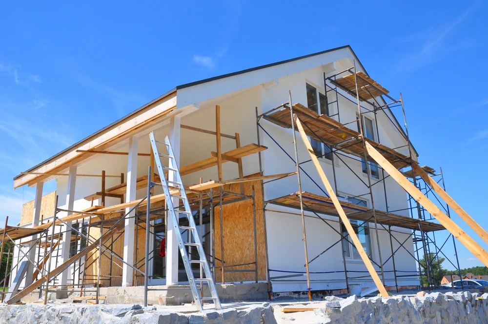 Chantier de construction résidentielle en cours, ouvriers travaillant sur structure bois avec échafaudages métalliques tubulaires