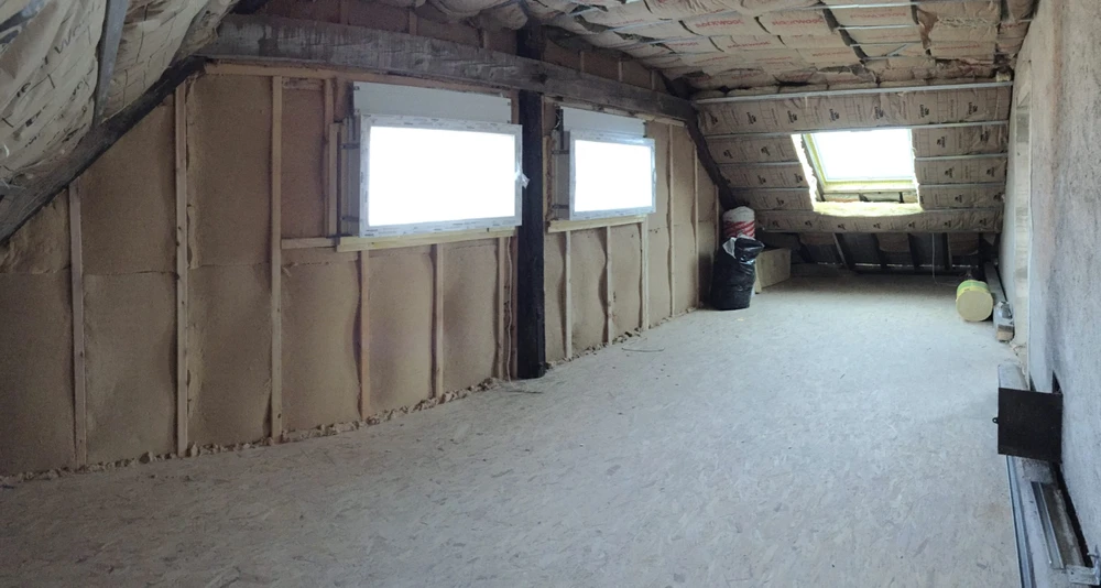 Combles aménageables en cours d'isolation, ouvrier installant laine minérale entre chevrons