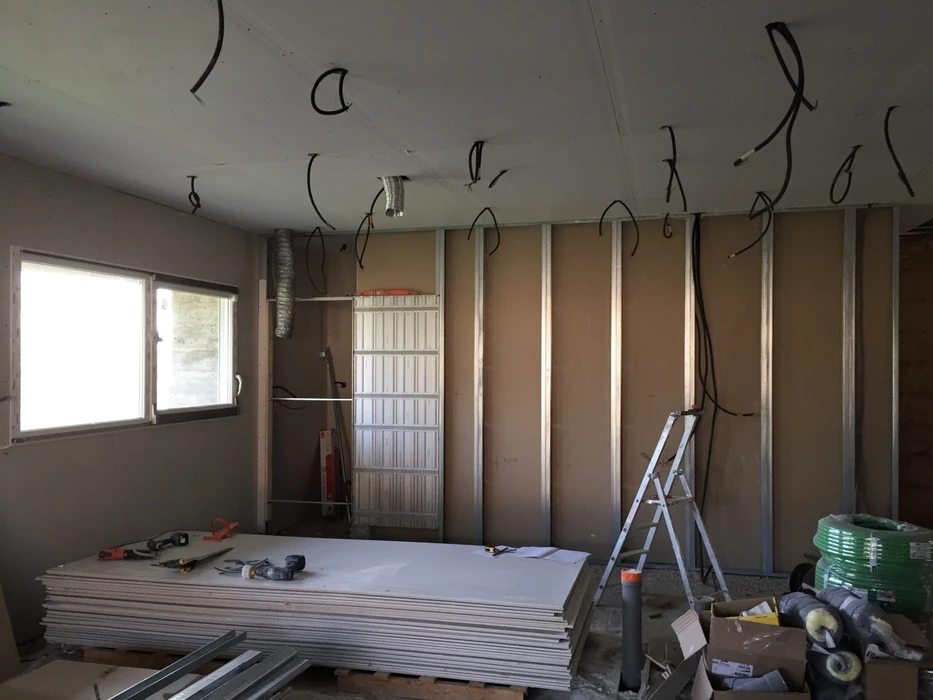 Couloir résidentiel en cours de rénovation avec ouvrier en vêtement rouge travaillant sur échelle pliante