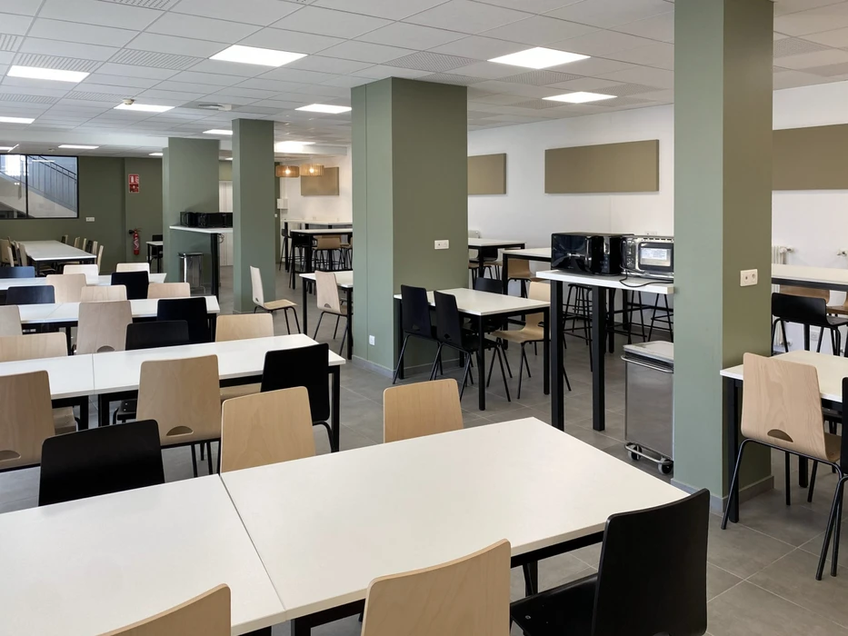 Espace de présentation commercial moderne avec cuisine ouverte équipée d'îlot central, tabourets hauts et grande table de réunion ovale