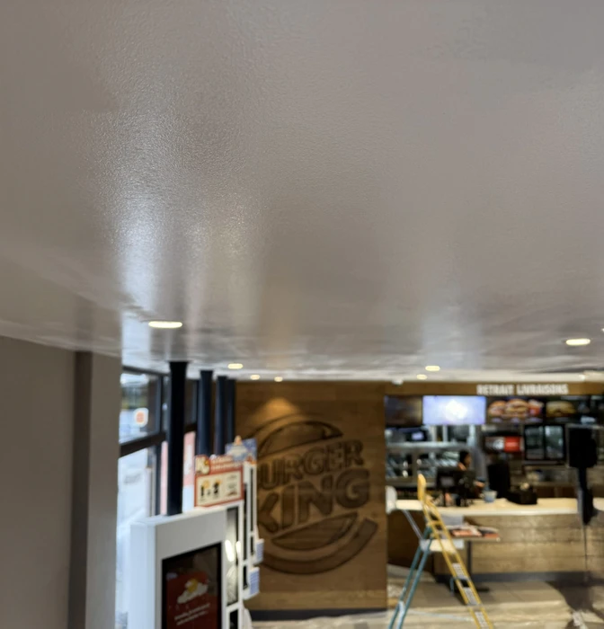 Espace de présentation commercial moderne avec cuisine ouverte équipée d'îlot central, tabourets hauts et grande table de réunion ovale