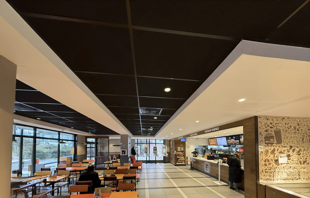 Espace de présentation commercial moderne avec cuisine ouverte équipée d'îlot central, tabourets hauts et grande table de réunion ovale