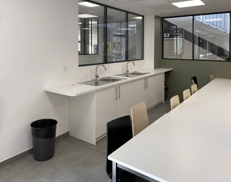 Espace de restauration d'entreprise moderne avec tables hautes et chaises, cuisine ouverte intégrée