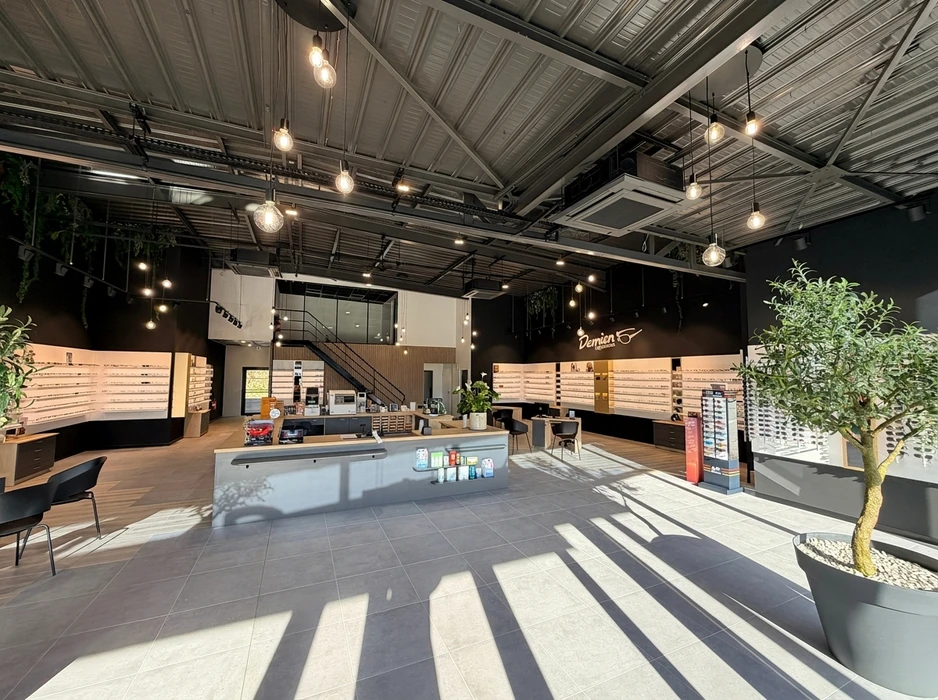 Espace de présentation commercial moderne avec cuisine ouverte équipée d'îlot central, tabourets hauts et grande table de réunion ovale