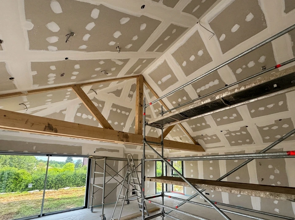 Chantier de construction extérieur, charpentier en casque jaune travaillant sur une structure en bois